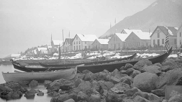 traditional dug out canoes on a rocky shore in front of houses lining the coast